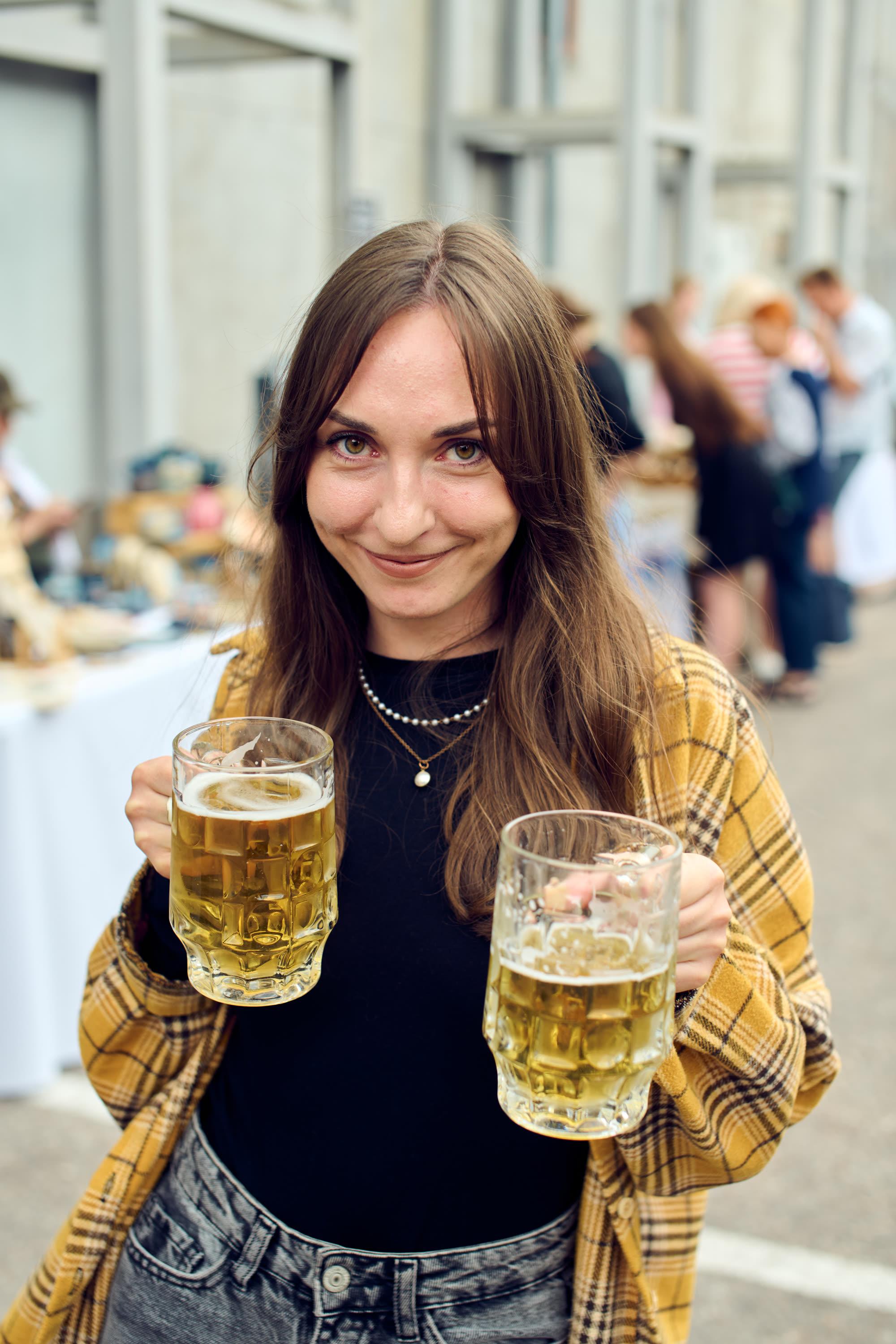 Una invitada sonriente con dos tarros de cerveza en un evento al aire libre